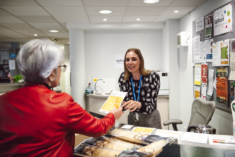 woman at desk handing another woman a flyer